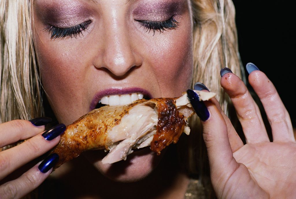 Young woman eating chicken leg, close up
