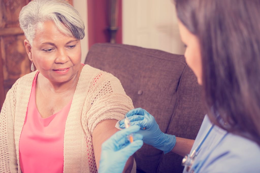 Home healthcare nurse giving injection to senior adult woman.
