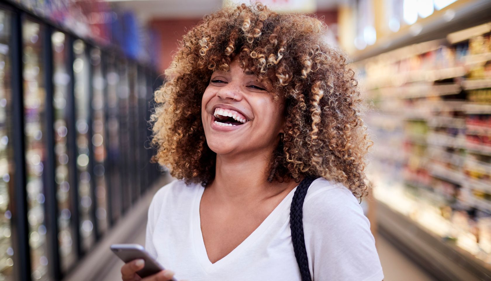 Black woman holding cell phone laughing in grocery store