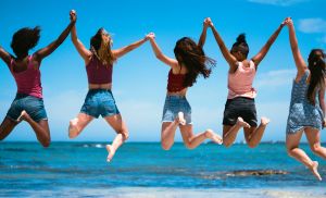 Female friends jumping against sea and sky