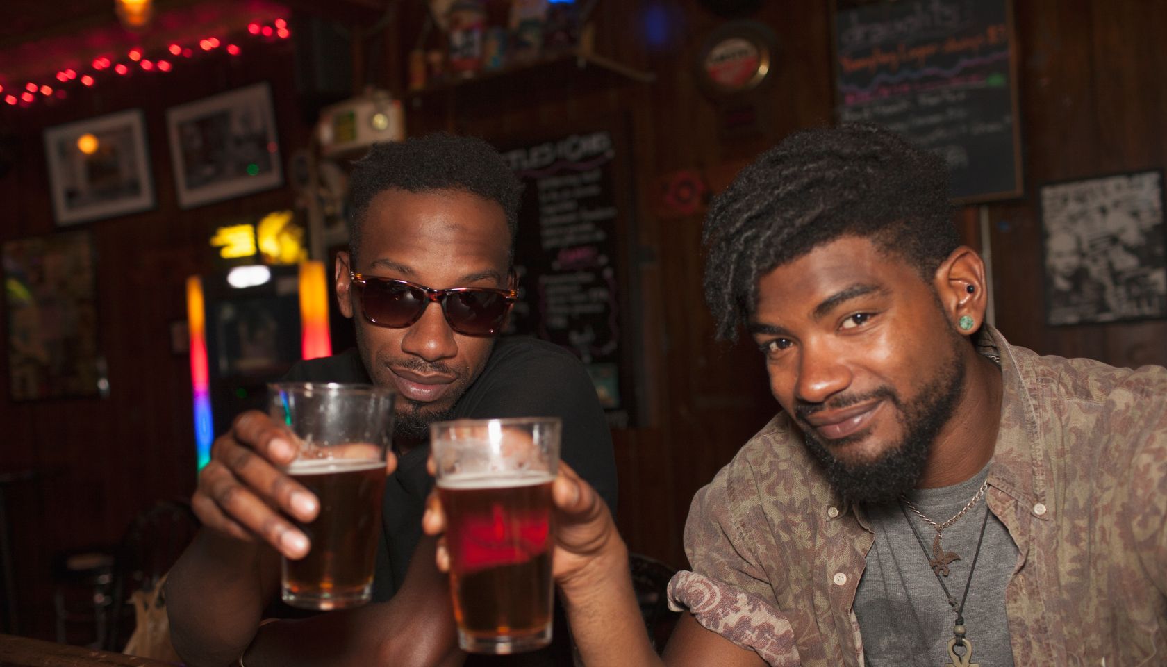 Two young men toasting at a bar.
