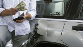 Man removing bank notes from wallet while refuelling car, mid section