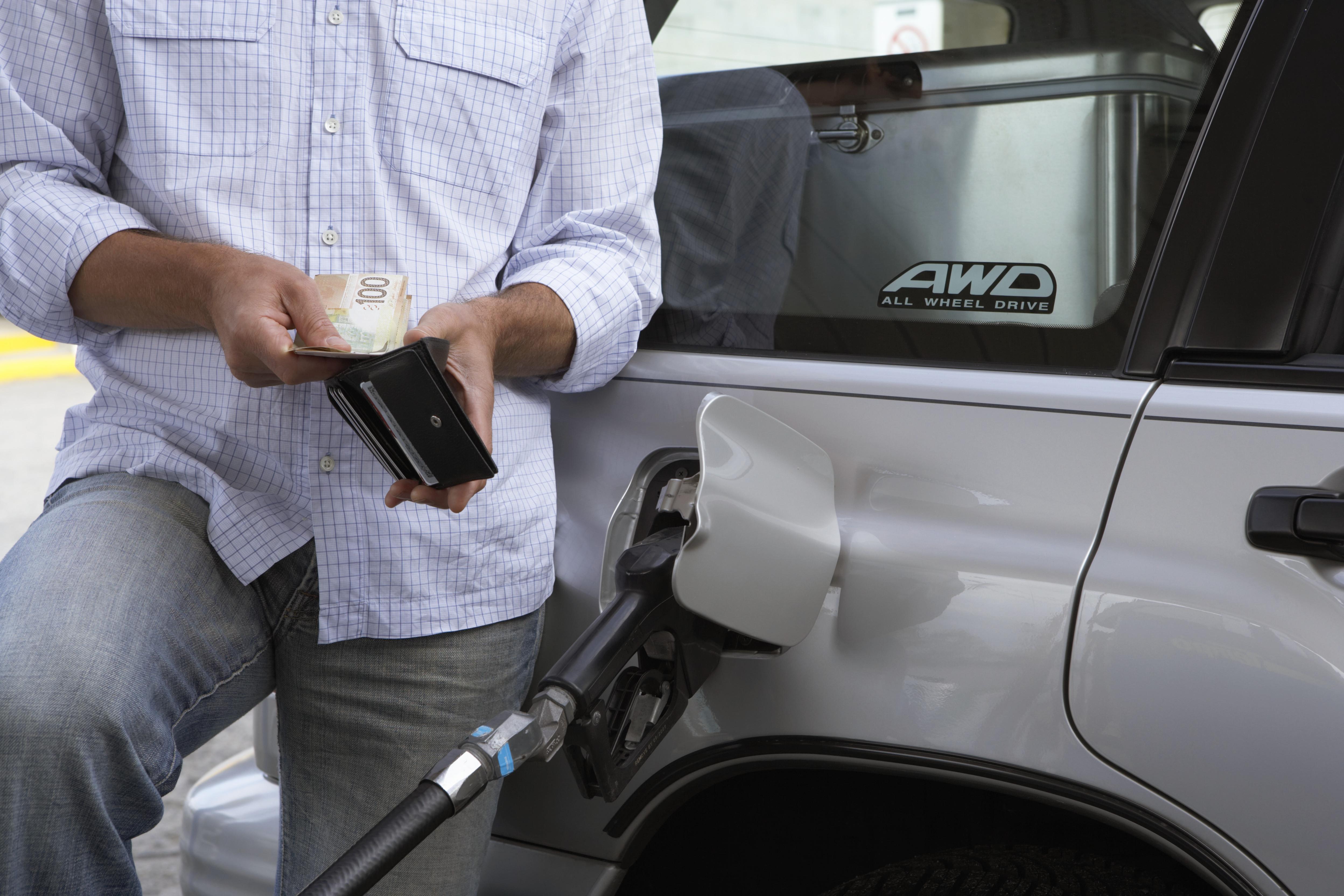 Man removing bank notes from wallet while refuelling car, mid section