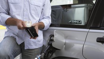 Man removing bank notes from wallet while refuelling car, mid section