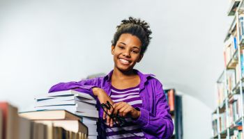 Pensive black girl in library posing with books