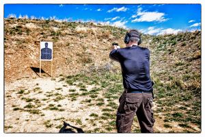 Man firing handgun at target outdoors.