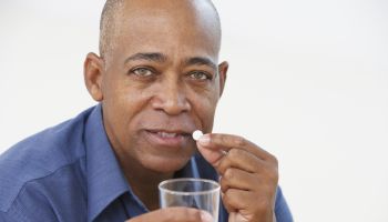 Senior African man taking medication with glass of water