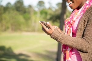 One African descent woman using cell phone outdoors in park.