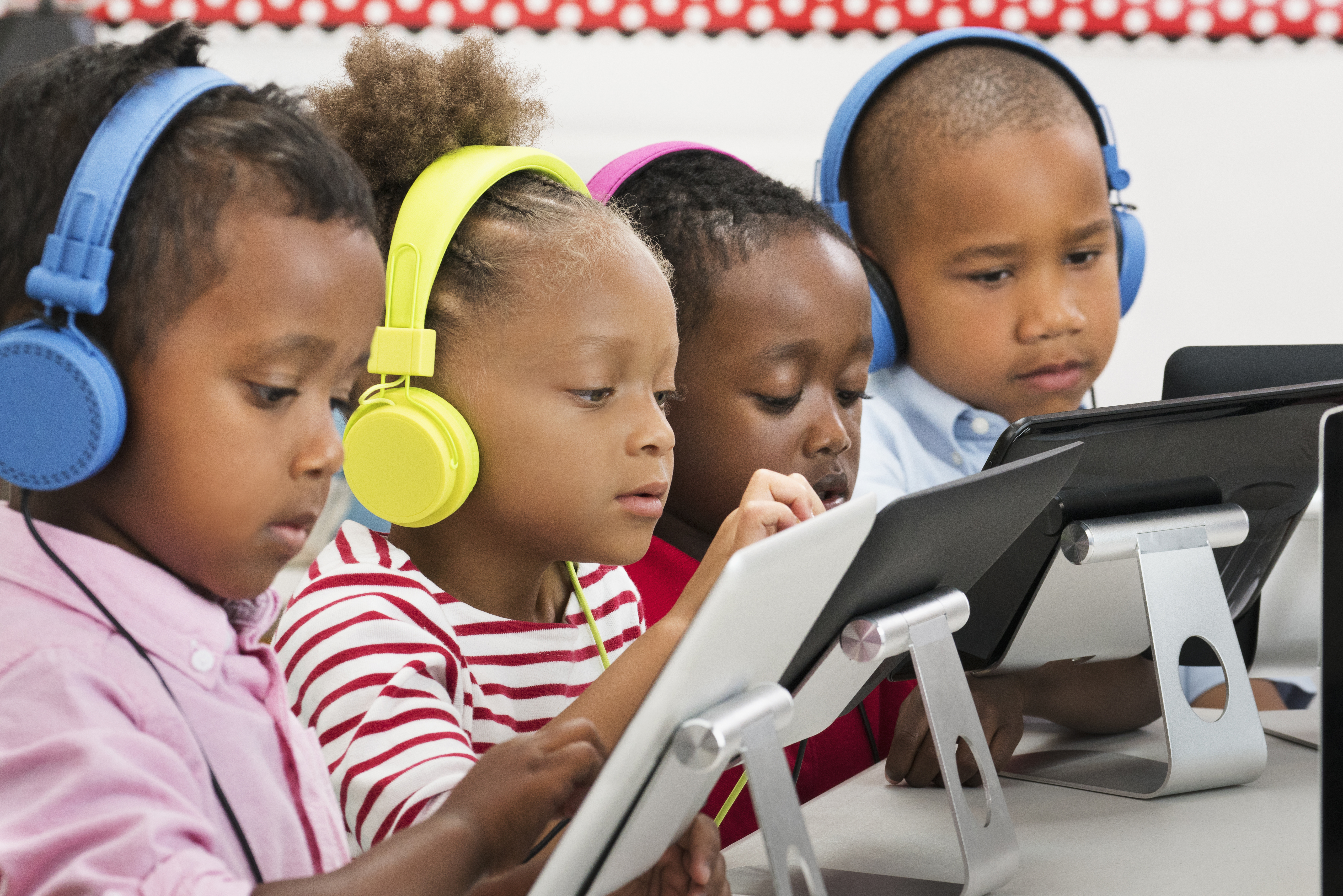 Students using digital tablets with headphones in classroom