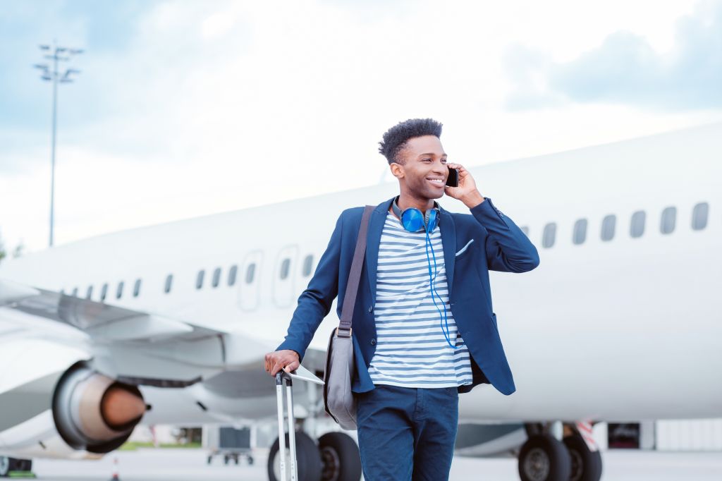 Young businessman talking on smart phone in front of airplane