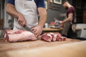 Male butcher with knife cutting into raw red meat in butcher