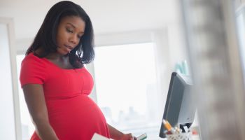 Black pregnant businesswoman reading paperwork at desk in office