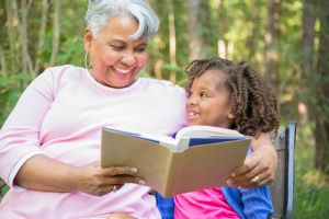 Grandmother and grandchild reading books outdoors together.