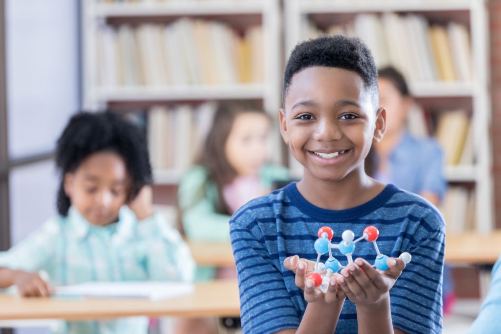 Preteen boy holds a molecular structure model for camera
