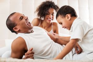 Cheerful African American family having fun in bed.