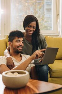 Happy African American couple surfing the net on laptop at home.