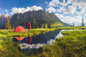 Camping with tent near high altitude lake on the Alps. Reflection of snowcapped mount Hochkönig range and scenic cloud sky