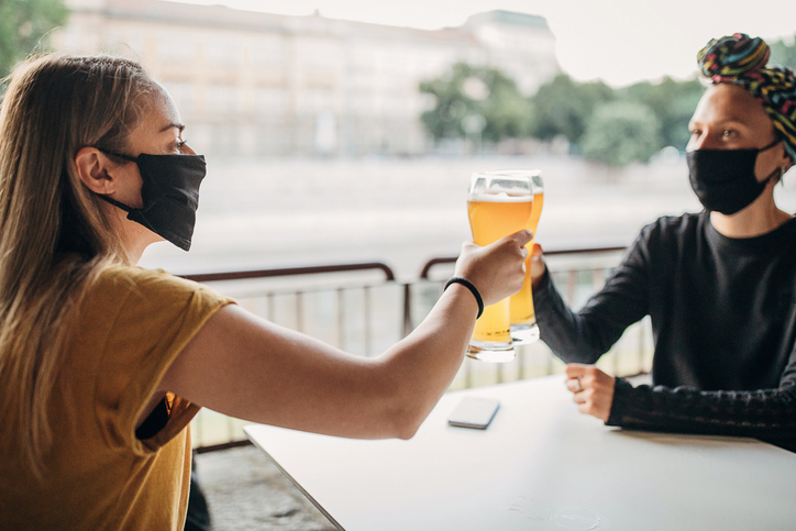 Two women with black face masks drinking beer in cafe outdoors