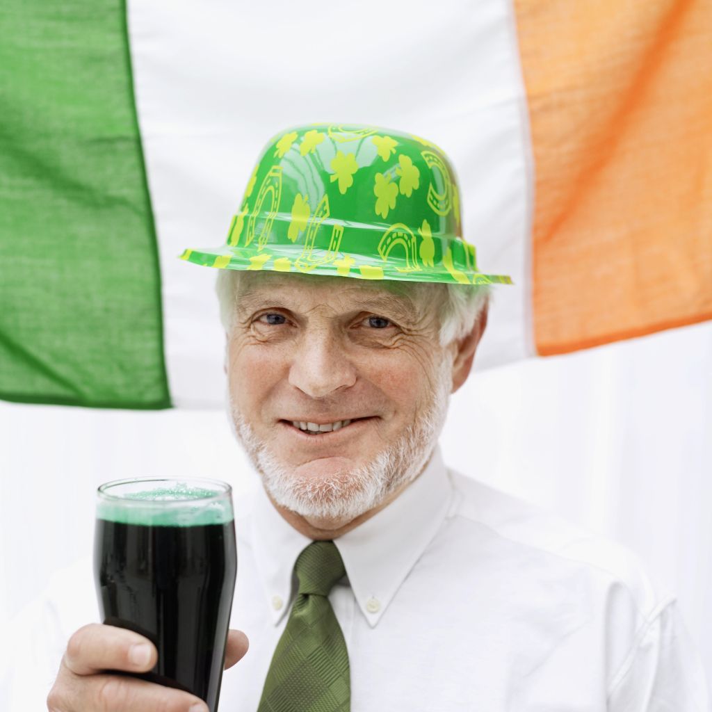 Elderly man dressed as a leprechaun holding a glass of stout