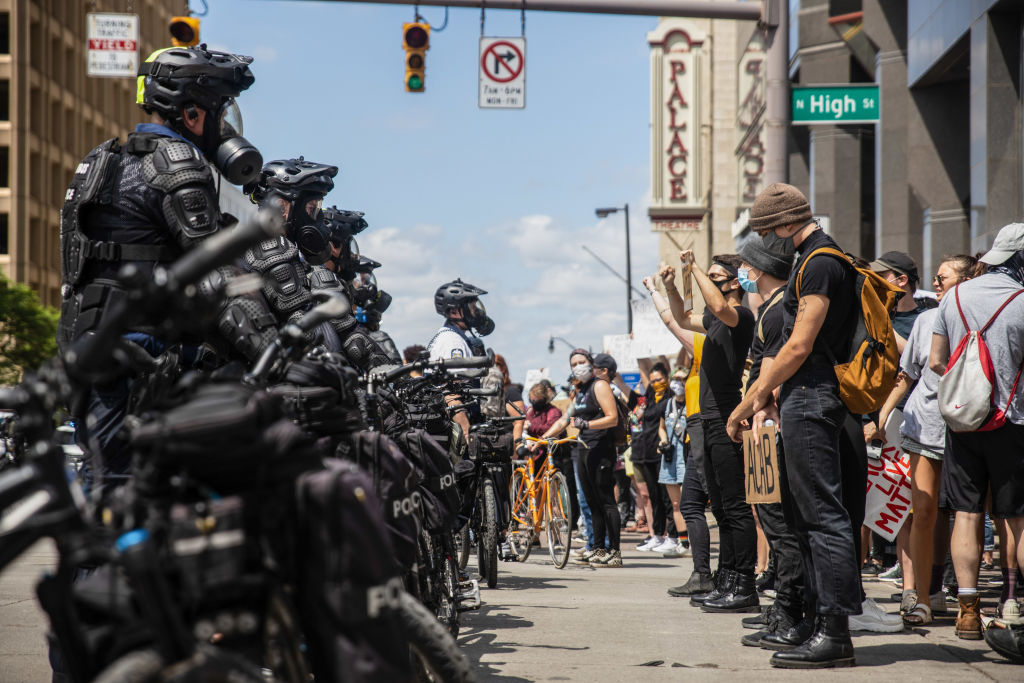 Protesters confront police officers standing in the middle...