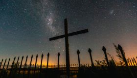 View of religious cross and fence against milky way in sky