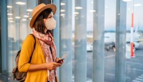 Young woman with mask looking the airport runway from the window