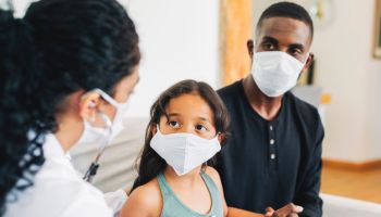 Doctor on house call examining small girl during pandemic