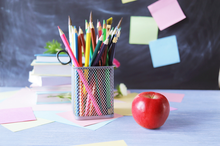 A stack of textbooks, multi-colored pencils, a red apple, on the background of a school board and note paper, educational supplies, education