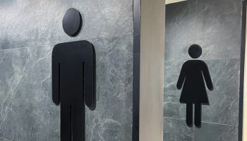 Close-up image of modern public toilet wall signs, black, men (gents) and women (ladies) symbols on grey, marble effect tiled public toilet wall