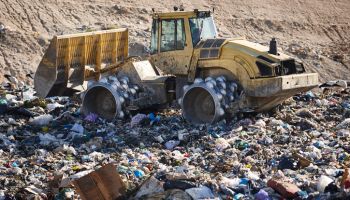 Heavy machinery shredding garbage in an open air landfill. Pollution