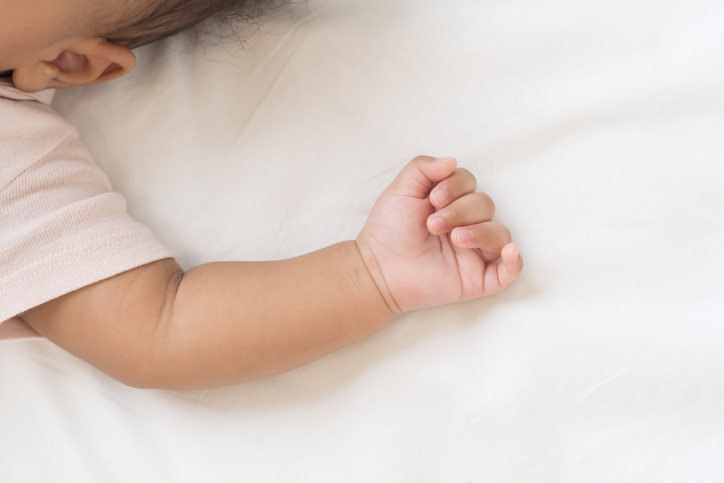 Newborn health care. Newborn baby sleeping on bed. Hands and soft skin of newbord baby during lying on white blanket