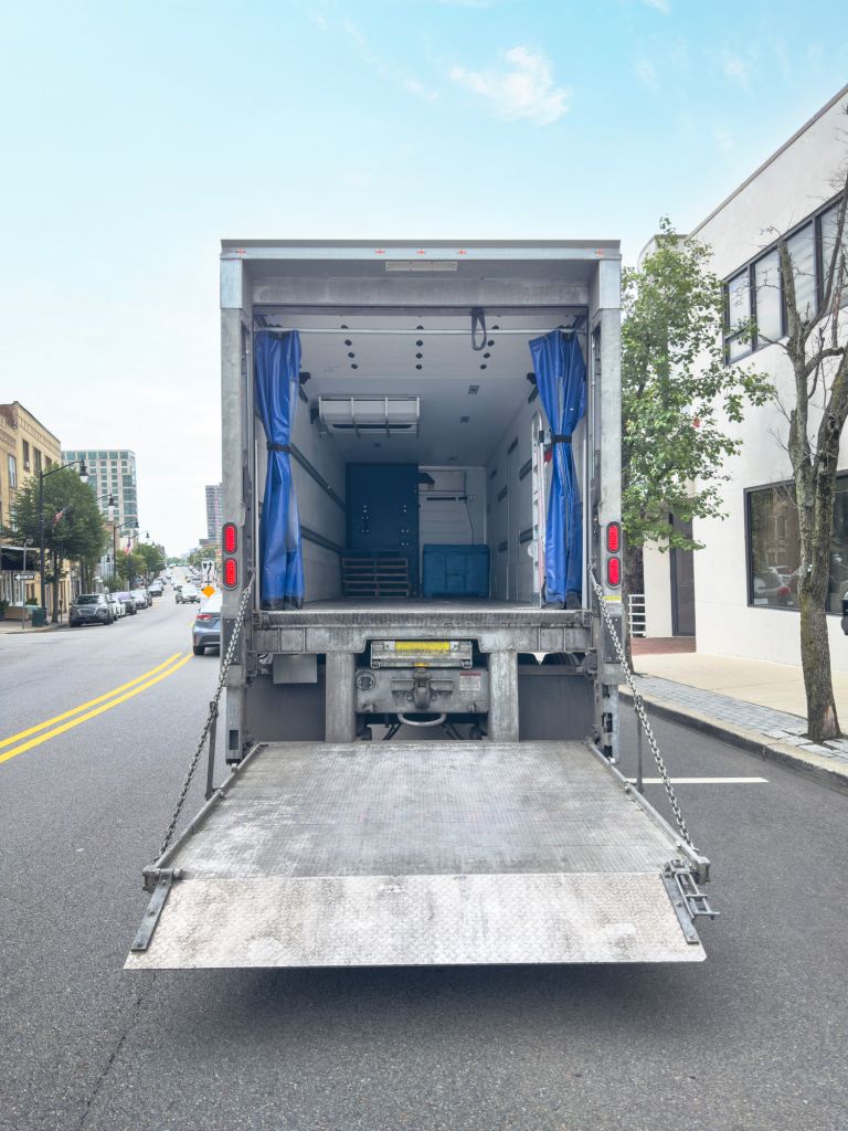 Empty moving truck with open cargo door parked on city street