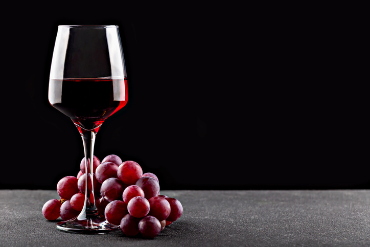 Elegant red wine glass beside fresh grapes on dark background with copy space for design