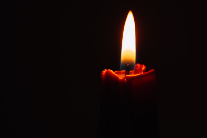 Close-up of a single lit candle glowing warmly in a dark room, creating a peaceful and serene atmosphere